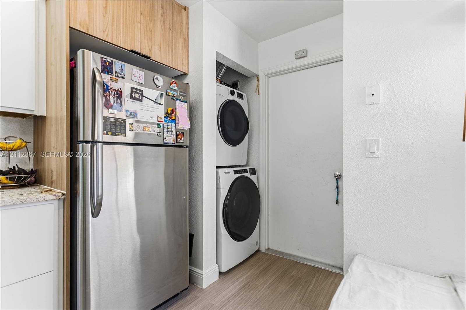 10803 Cypress Glen Drive, #10803, Coral Springs, FL 33071 Stainless steel refrigerator with overhead custom cabinetry, stacked front-load laundry appliances, and wood-finish flooring