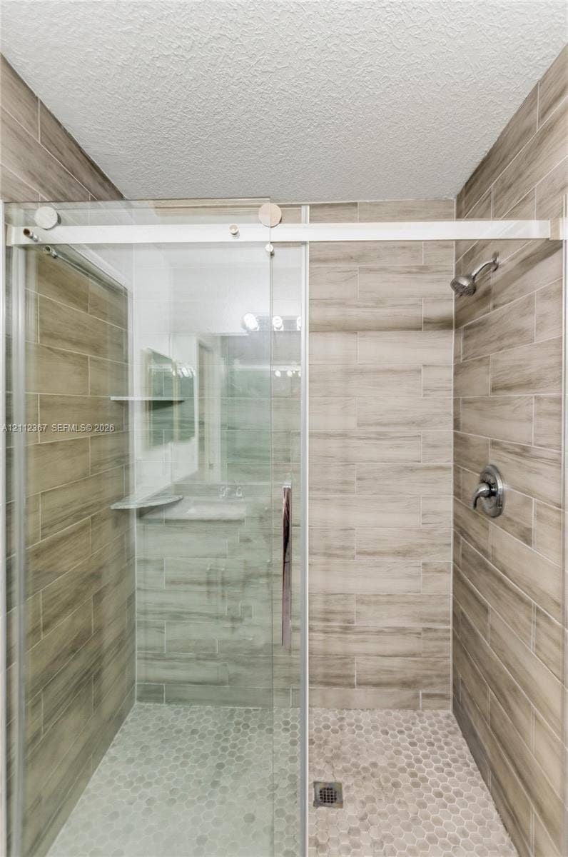10803 Cypress Glen Drive, #10803, Coral Springs, FL 33071 Walk-in shower featuring wood-finish tile surround, sliding glass door with stainless steel hardware, integrated corner shelving, and circular mosaic tile flooring
