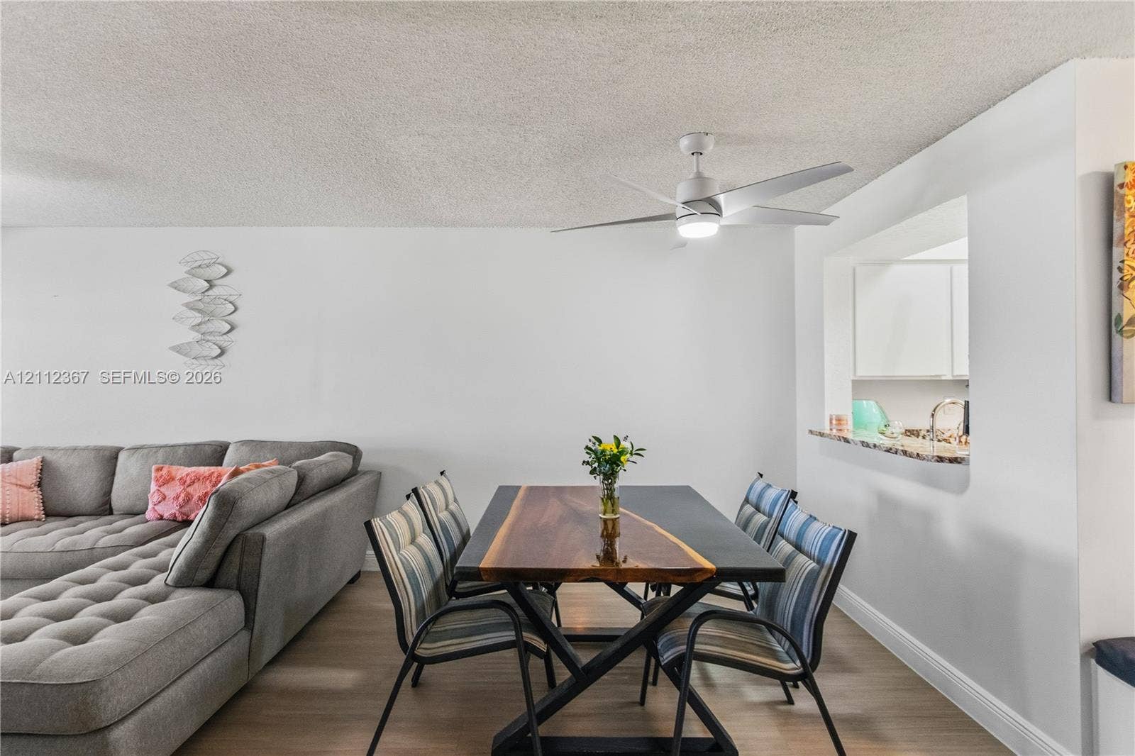 10803 Cypress Glen Drive, #10803, Coral Springs, FL 33071 Neutral interior space featuring wood-finish flooring, a contemporary white ceiling fan with integrated lighting, and a kitchen pass-through window with a stone-surface counter