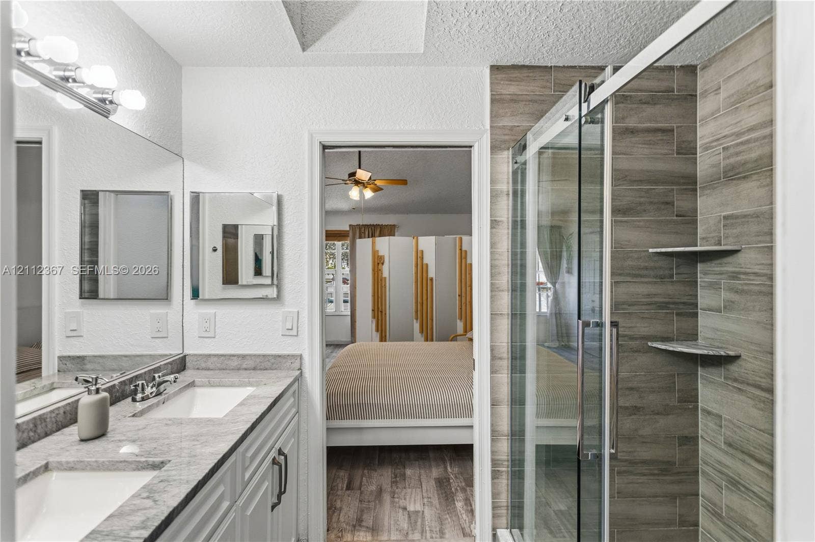10803 Cypress Glen Drive, #10803, Coral Springs, FL 33071 Dual-sink vanity with stone-finish countertop, full-width wall mirror, and walk-in shower with horizontal tile surround and integrated shelving