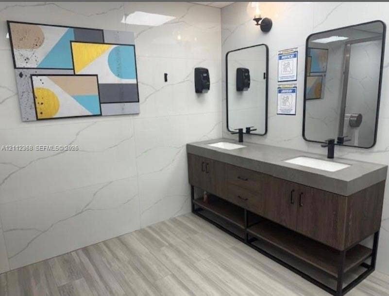 Double vanity featuring a thick concrete-style countertop with integrated sinks, wood-finish base cabinetry, large wall-mounted rectangular mirrors with matte black frames, and full-height veined tile wall surfacing