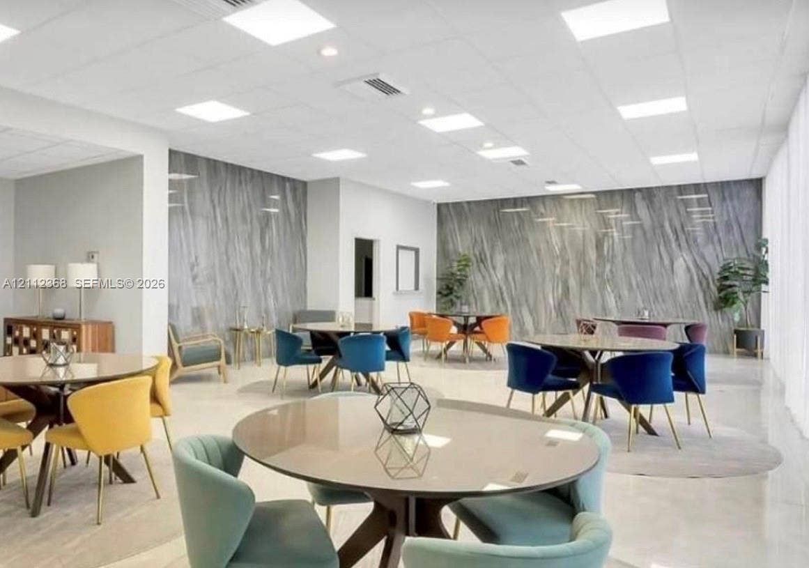 Open-concept interior featuring large-format polished flooring, drop ceiling with recessed panel lighting, and floor-to-ceiling stone-finish accent walls