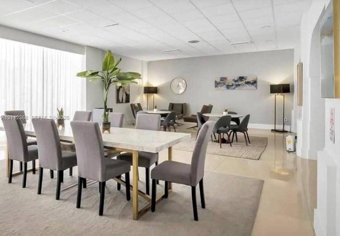 Open-concept room featuring a drop ceiling, expansive windows with floor-to-ceiling sheer drapery, and polished tile flooring