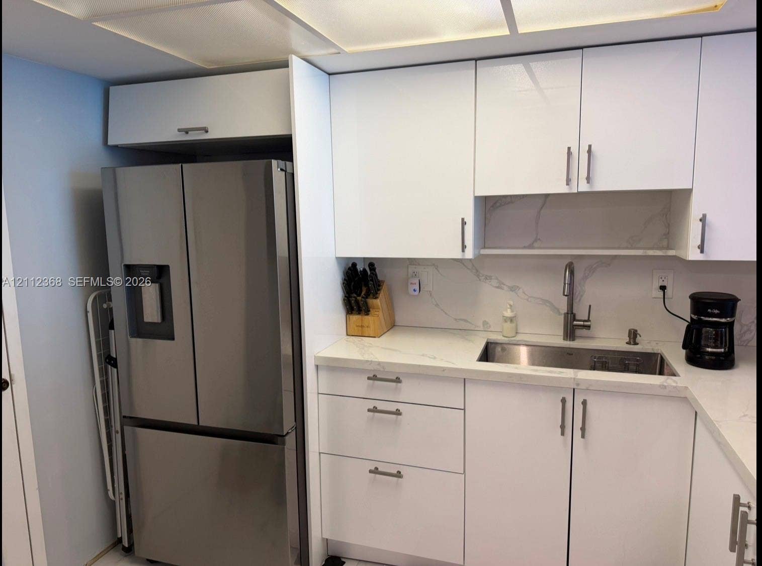 Kitchen featuring white slab-front cabinetry, stone-finish countertops, full-height stone-finish backsplash, stainless steel under-mount sink, and stainless steel French-door refrigerator