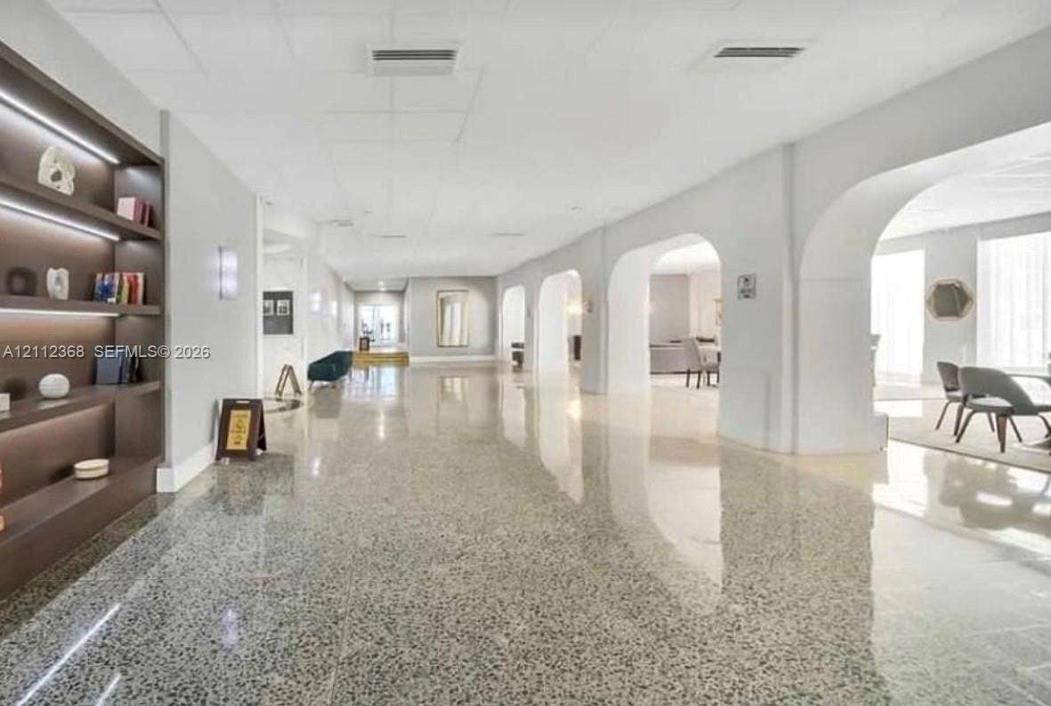 Spacious hallway featuring polished terrazzo flooring, integrated recessed shelving with ambient lighting, and decorative arched architectural openings