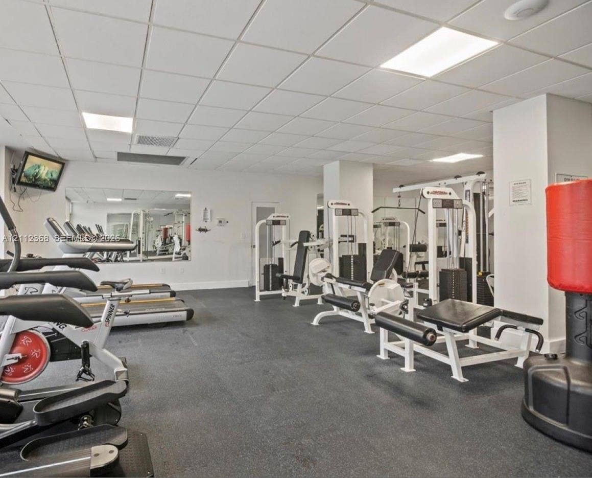 Fitness area featuring drop ceiling panels, recessed lighting, wall-to-wall mirrors, and durable rubber flooring
