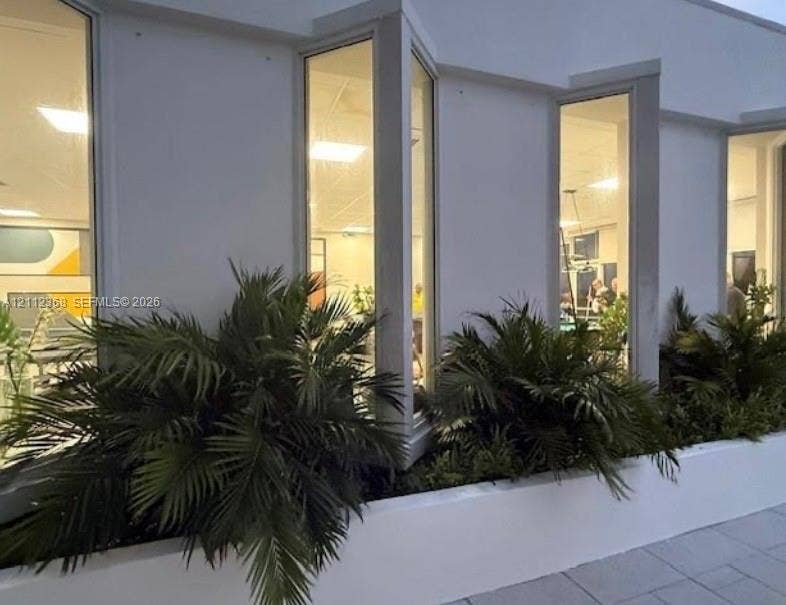 Smooth stucco exterior featuring floor-to-ceiling vertical windows and a built-in concrete planter with mature palm greenery
