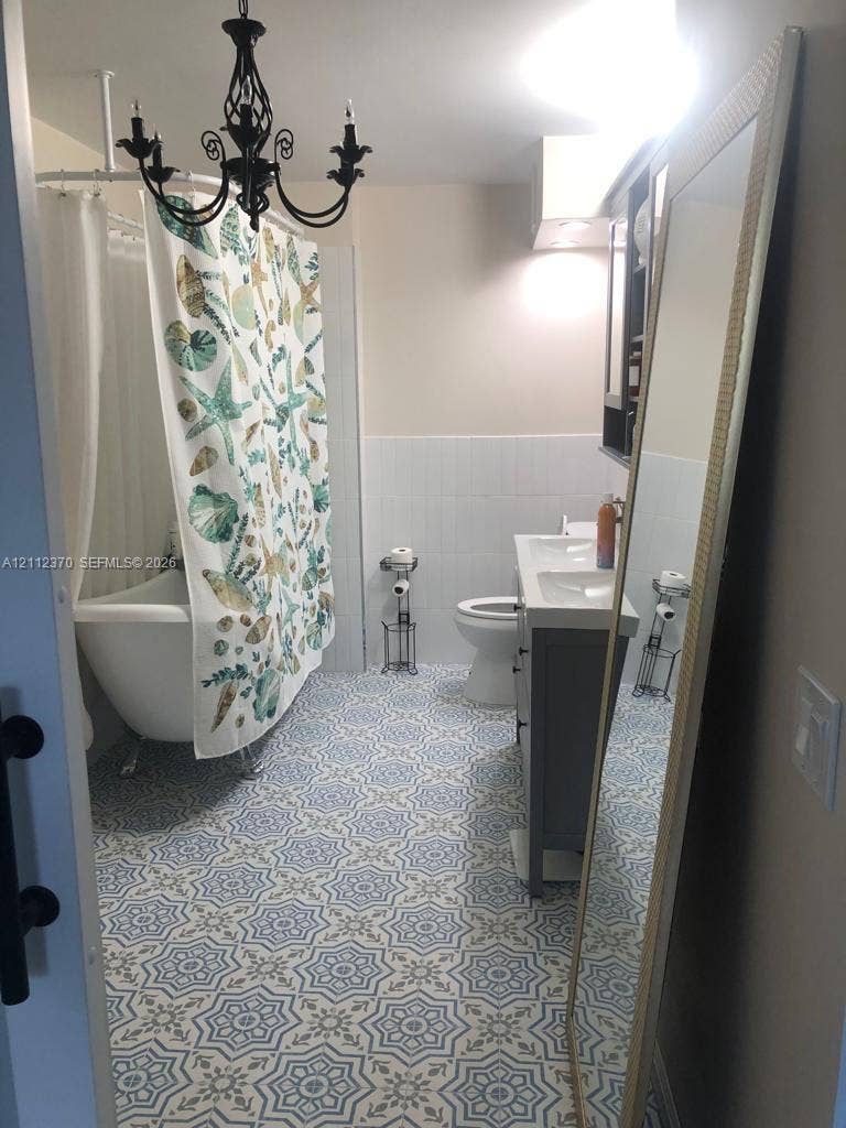 Clawfoot tub, patterned tile flooring, dual-basin vanity with gray cabinetry, and decorative wrought-iron chandelier