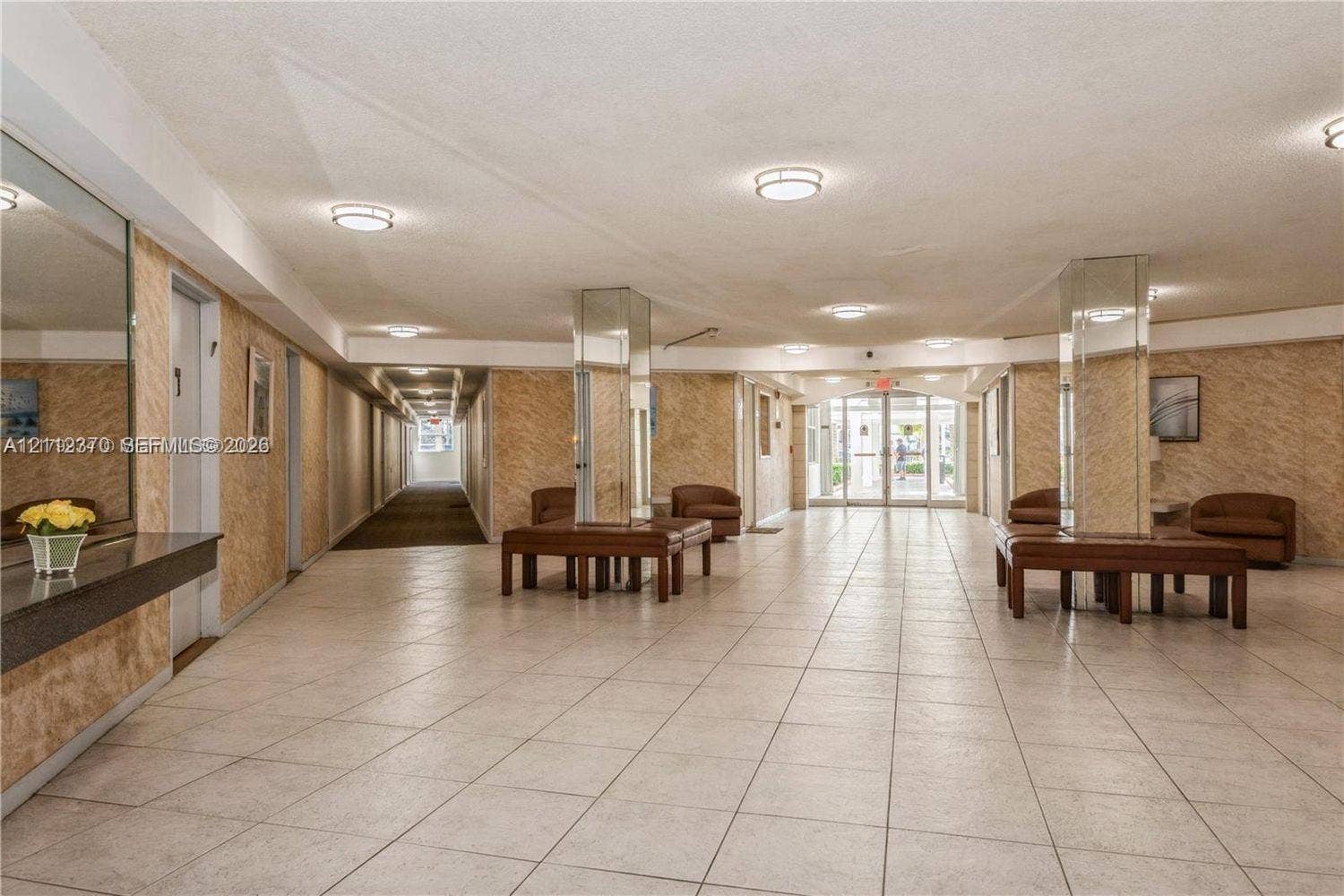 Common area featuring large-format tile flooring, mirrored structural pillars, textured wall surfaces, recessed ceiling lighting, and a glass-paneled entry door