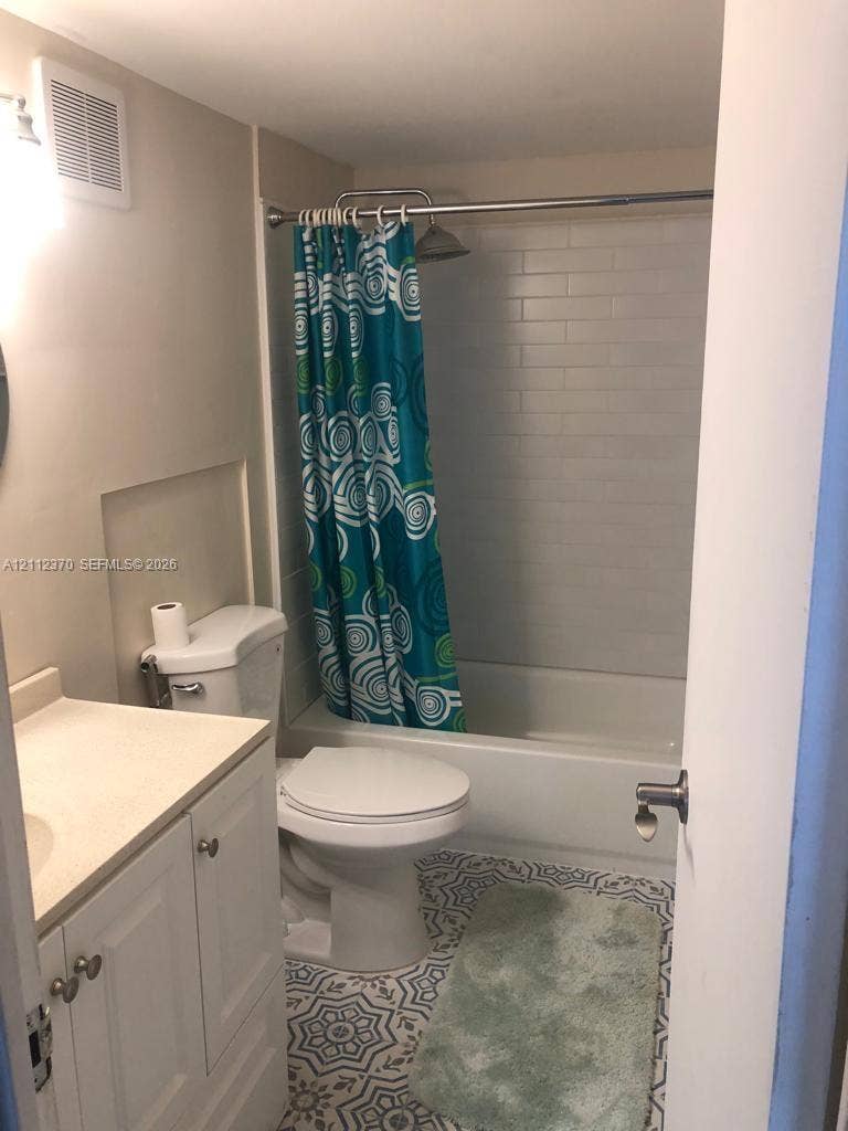 Bathroom featuring a vanity with a solid-surface countertop, tub-shower combination with white subway-style wall tile, and patterned ceramic floor tiling