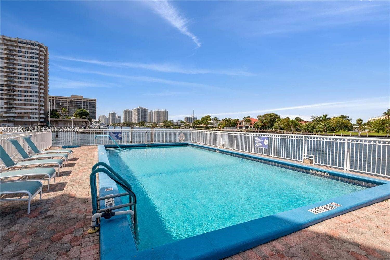 Rectangular swimming pool featuring a brick-paver deck and white metal fencing