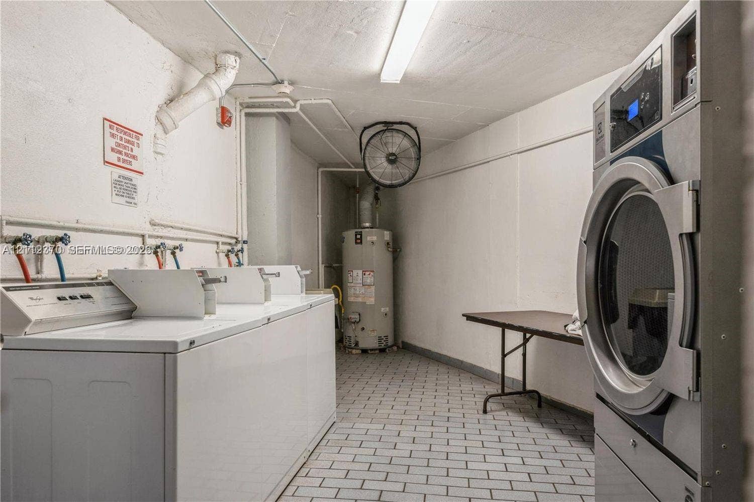 Laundry area featuring multiple washing machines, a large-capacity dryer, a dedicated water heater, and tiled flooring