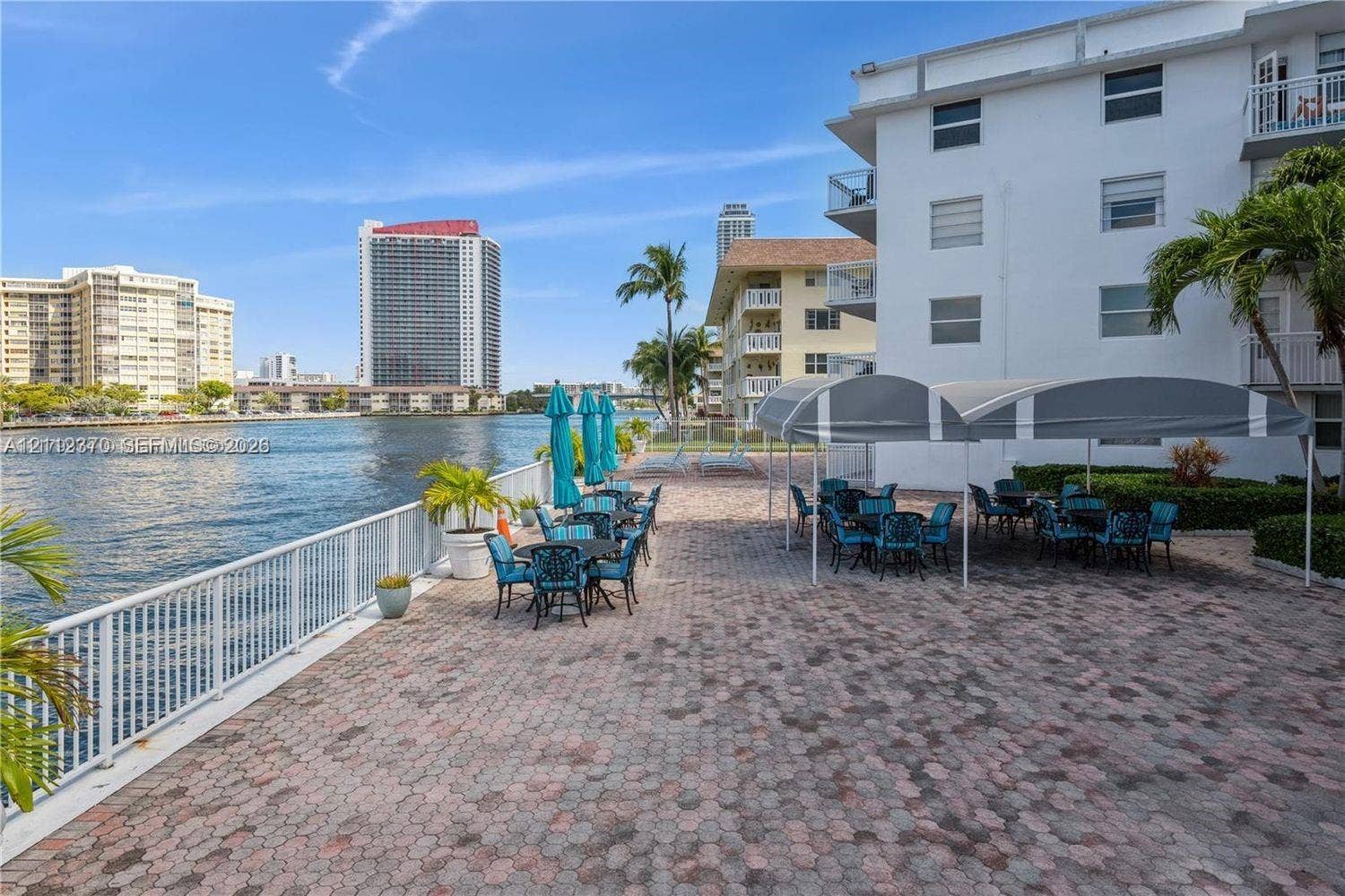Waterfront terrace featuring stone paver flooring, white metal railing, and arched fabric awnings