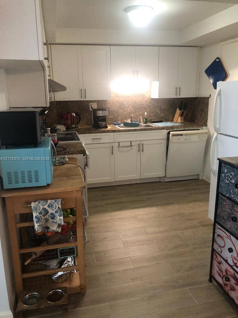 Kitchen featuring white cabinetry, stone-surface countertops, a stainless steel sink, integrated dishwasher, and wood-finish tile flooring