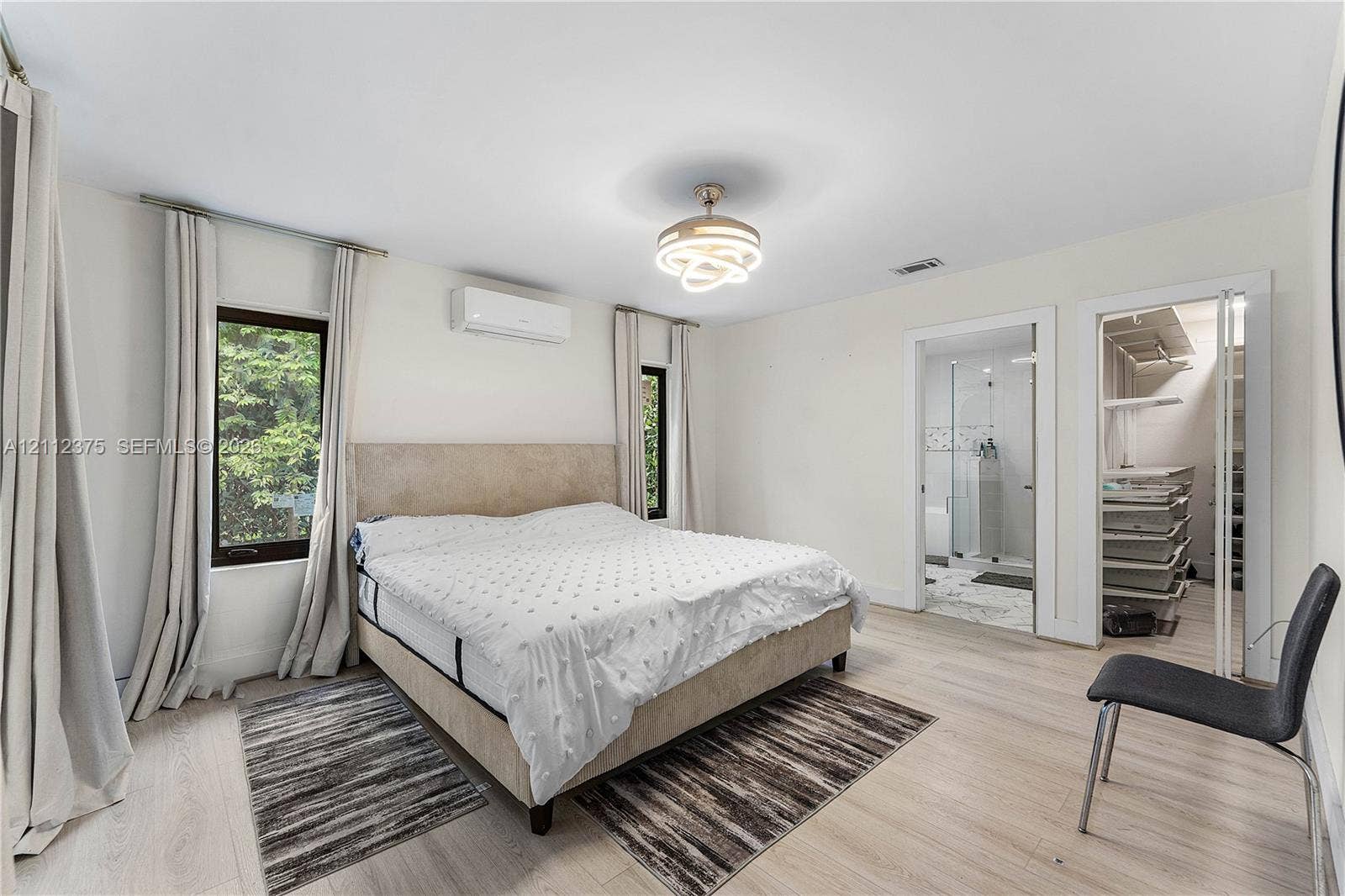 10936 NW 41st Drive, Coral Springs, Coral Springs, FL 33065 Light-filled room featuring wood-finish flooring, a wall-mounted ductless climate control unit, a modern multi-ring circular light fixture, and walk-in closet with custom shelving