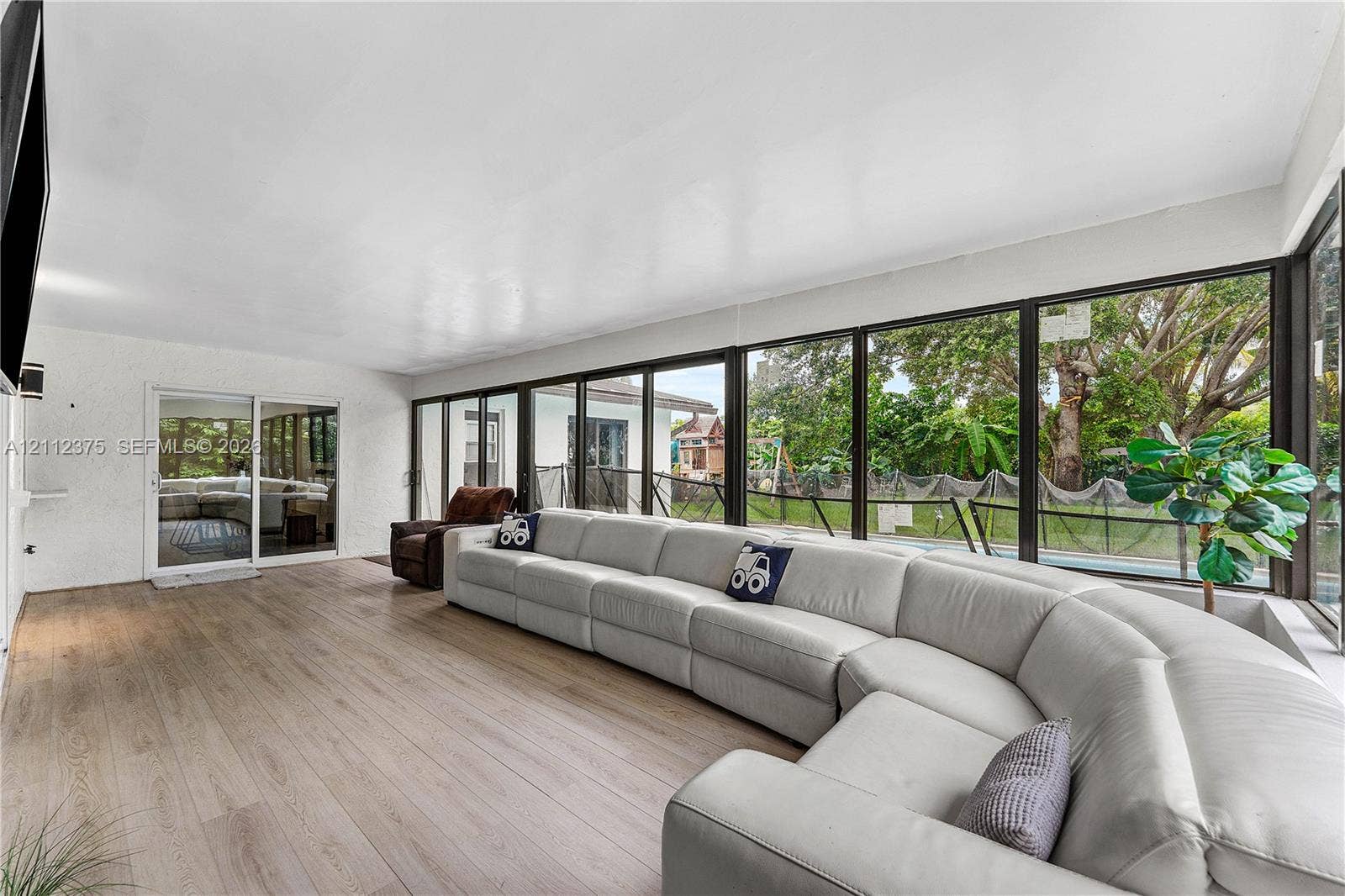 10936 NW 41st Drive, Coral Springs, Coral Springs, FL 33065 Expansive sunroom featuring full-height walls of glass, wood-finish flooring, and sliding glass door access to the exterior