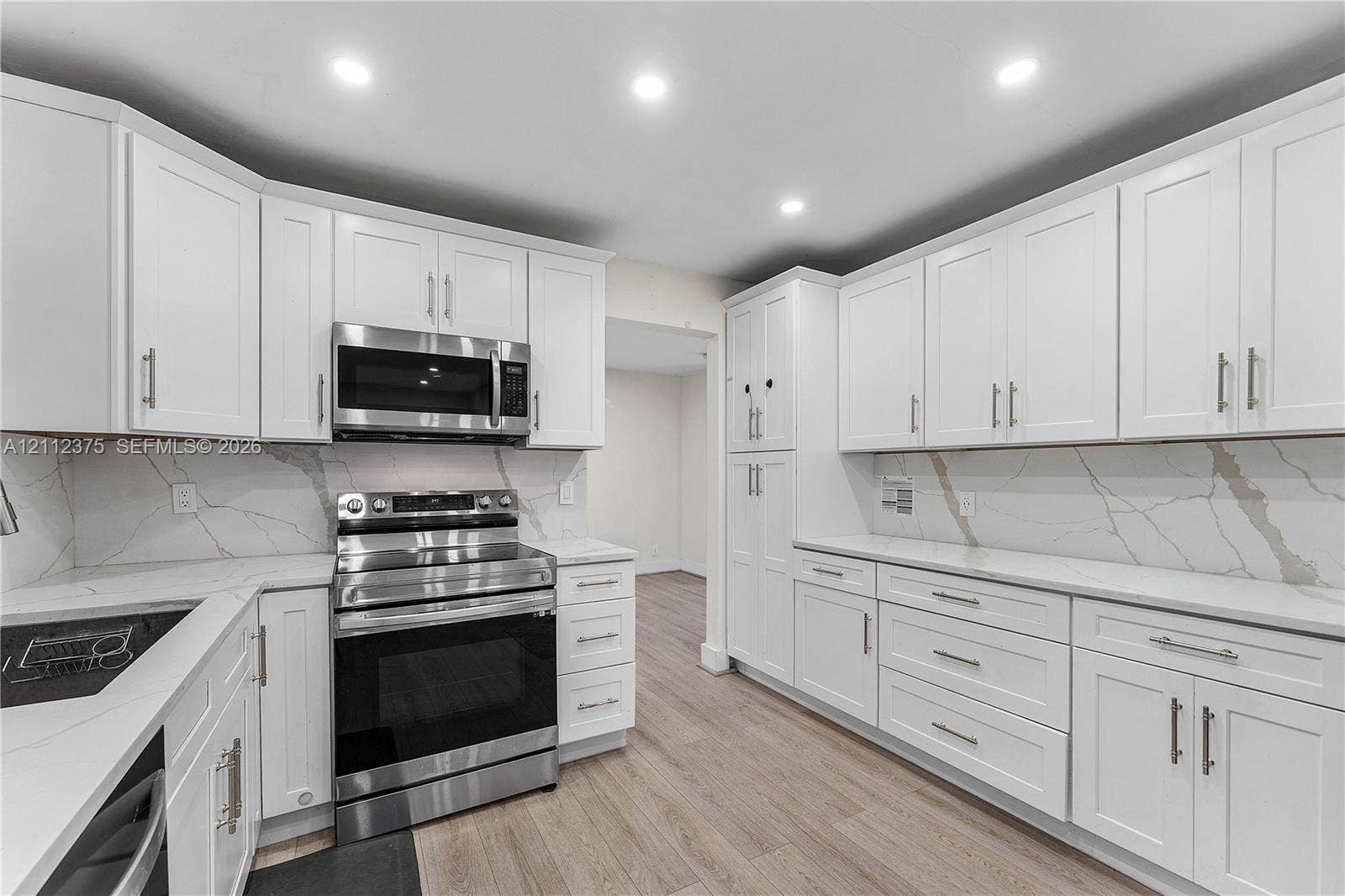 10936 NW 41st Drive, Coral Springs, Coral Springs, FL 33065 Kitchen featuring white Shaker-style cabinetry, stainless steel appliances, stone-patterned backsplash, quartz countertops, and wood-finish flooring