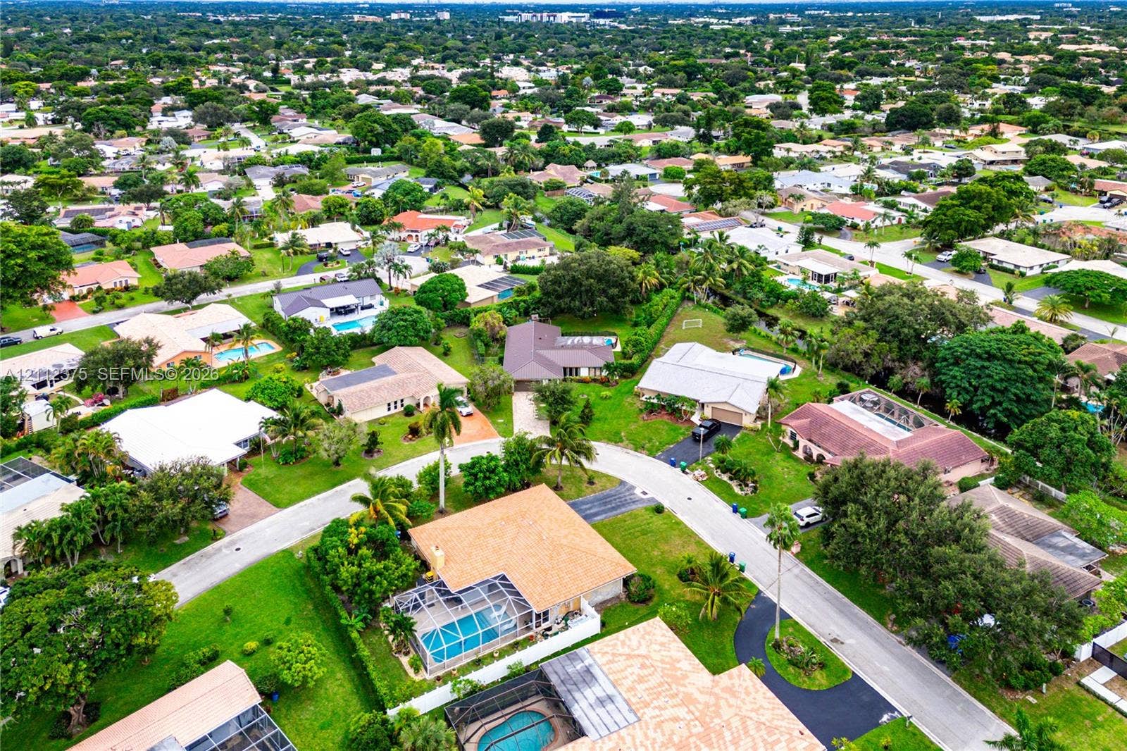 10936 NW 41st Drive, Coral Springs, Coral Springs, FL 33065 Aerial perspective of the residential property featuring a screened-in swimming pool, shingled roofing, paved driveway, and mature landscaping within a suburban setting