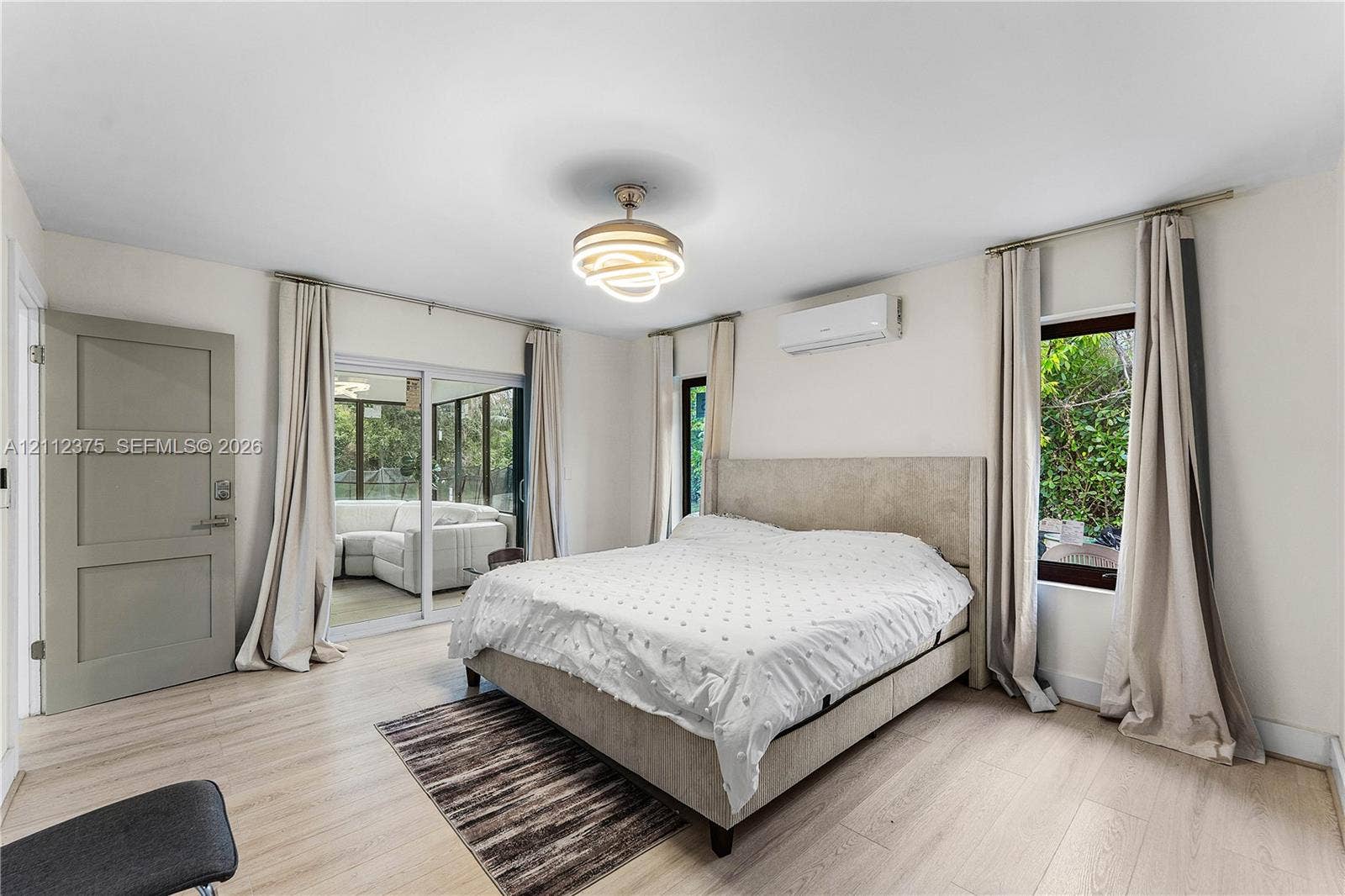 10936 NW 41st Drive, Coral Springs, Coral Springs, FL 33065 Light-toned wood-finish flooring, modern circular tiered ceiling light fixture, wall-mounted ductless air conditioning unit, sliding glass doors, and a solid-panel interior door
