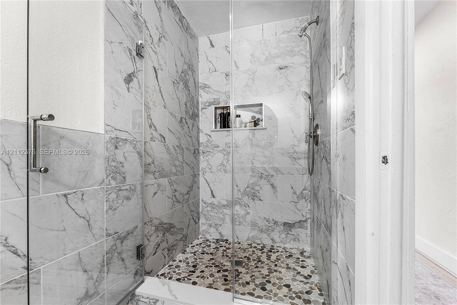 10936 NW 41st Drive, Coral Springs, Coral Springs, FL 33065 Walk-in shower featuring floor-to-ceiling stone-pattern tile, a glass enclosure, a pebble-finish floor, a recessed wall niche, and a handheld showerhead fixture