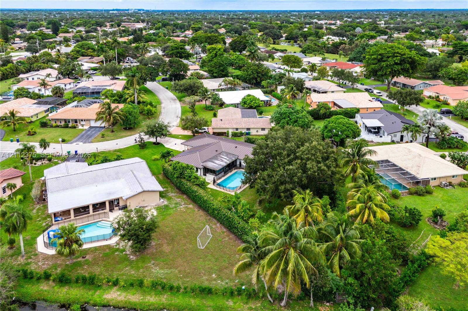 10936 NW 41st Drive, Coral Springs, Coral Springs, FL 33065 Aerial perspective of a suburban neighborhood featuring single-story residences with tiled roofs, screened-in swimming pools, expansive green lawns, and mature landscaping
