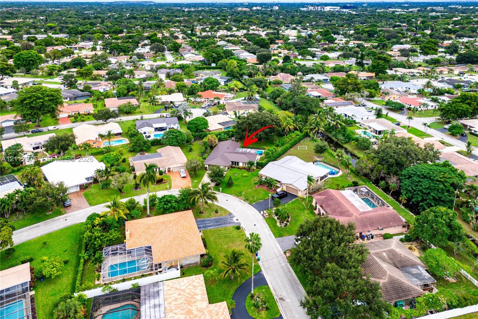 10936 NW 41st Drive, Coral Springs, Coral Springs, FL 33065 Aerial perspective of a single-story residence featuring a shingled roof, an in-ground swimming pool with a screened enclosure, a sprawling lawn, and mature perimeter landscaping