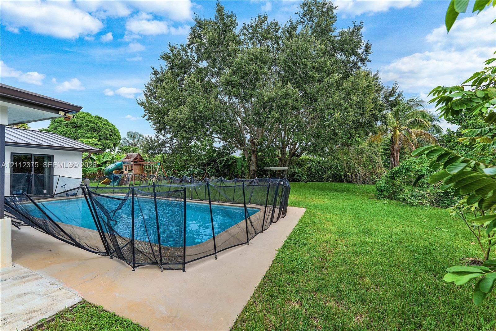 10936 NW 41st Drive, Coral Springs, Coral Springs, FL 33065 Rear exterior featuring a swimming pool, concrete patio, mature trees, and expansive lawn