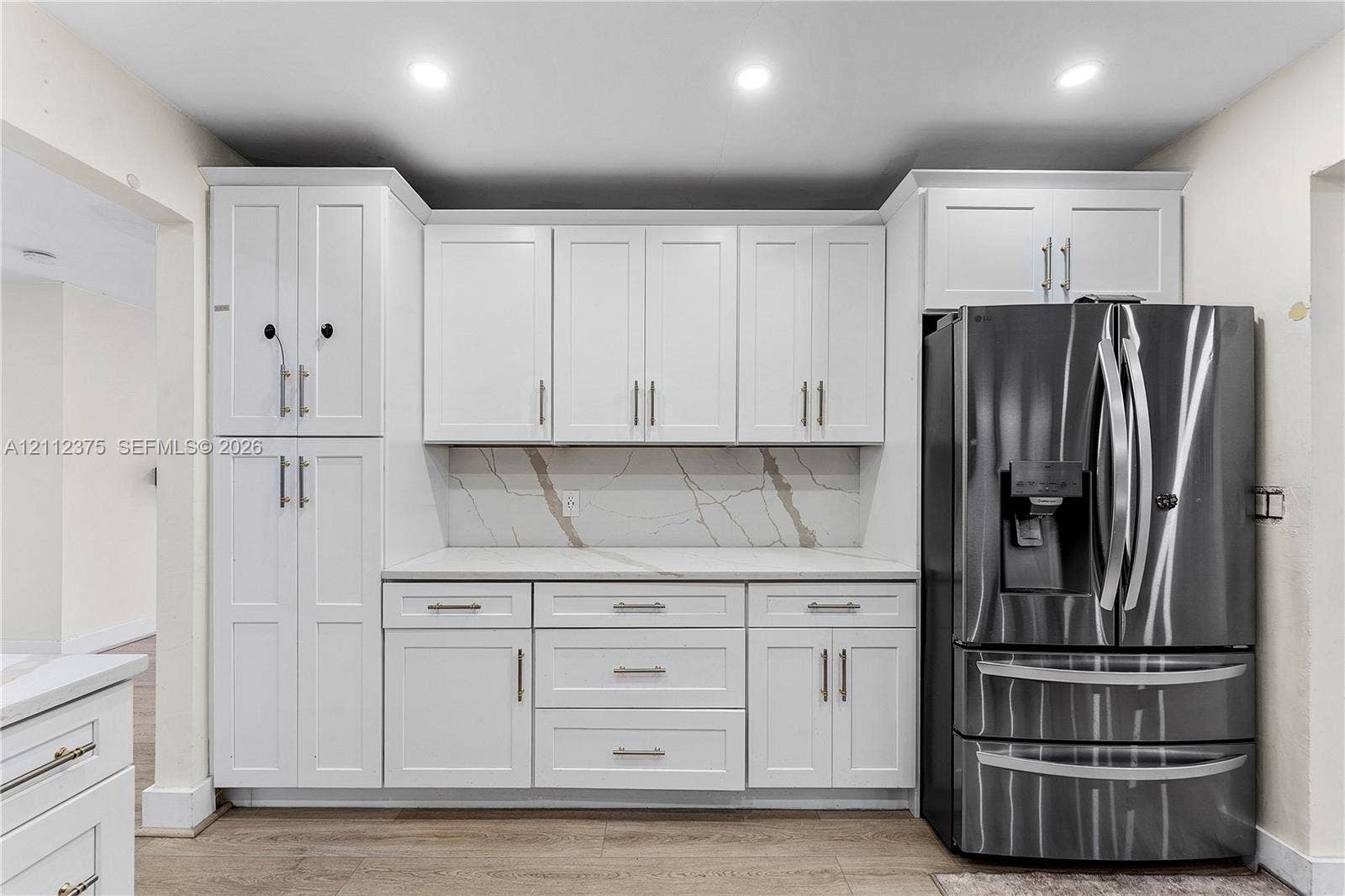 10936 NW 41st Drive, Coral Springs, Coral Springs, FL 33065 White shaker-style cabinetry with matte black hardware, stone-patterned backsplash, quartz countertops, stainless steel French door refrigerator, and wood-finish flooring