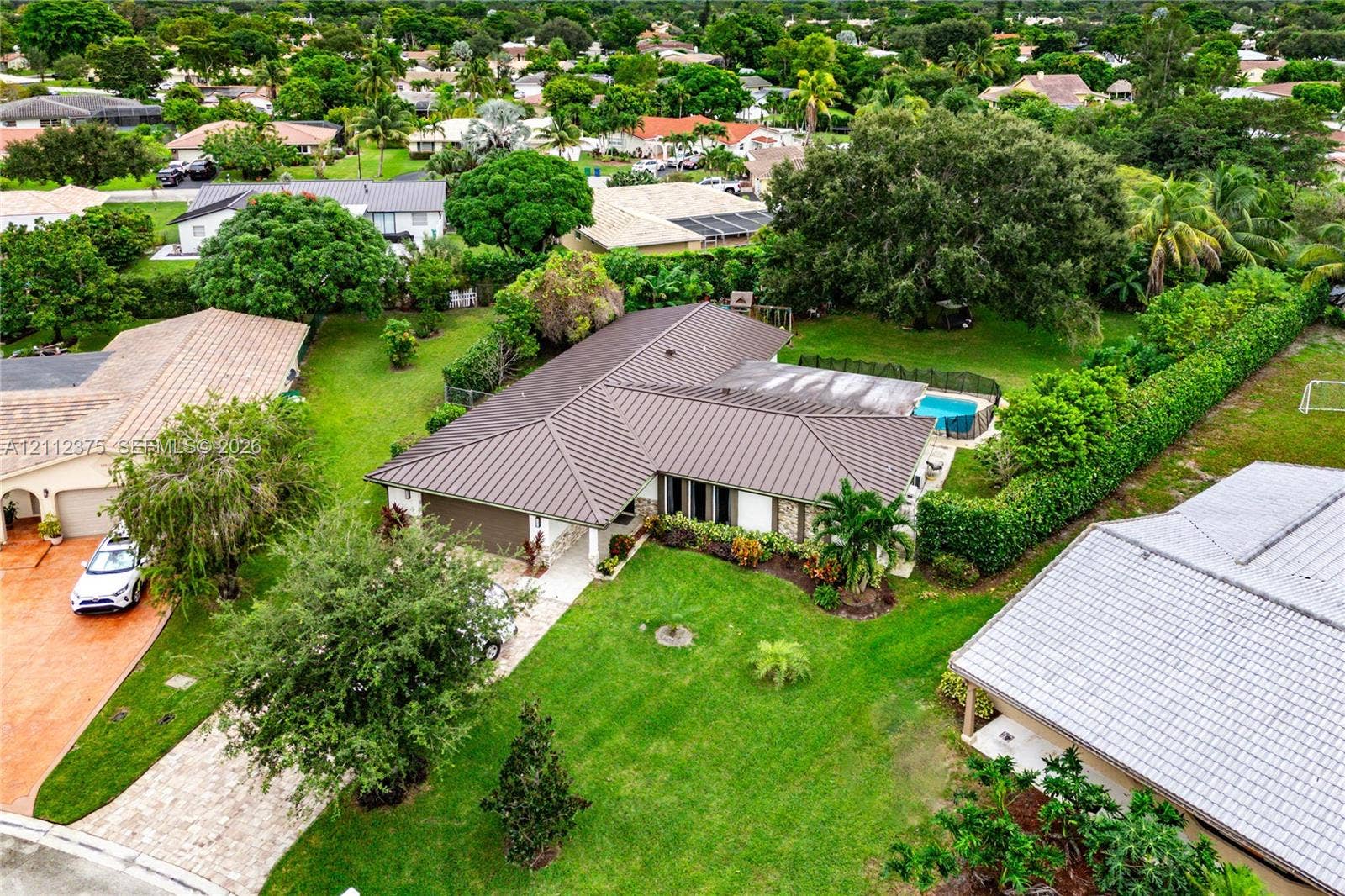 10936 NW 41st Drive, Coral Springs, Coral Springs, FL 33065 Aerial view featuring a metal roof, expansive grass lawn, mature landscaping, and a fenced swimming pool