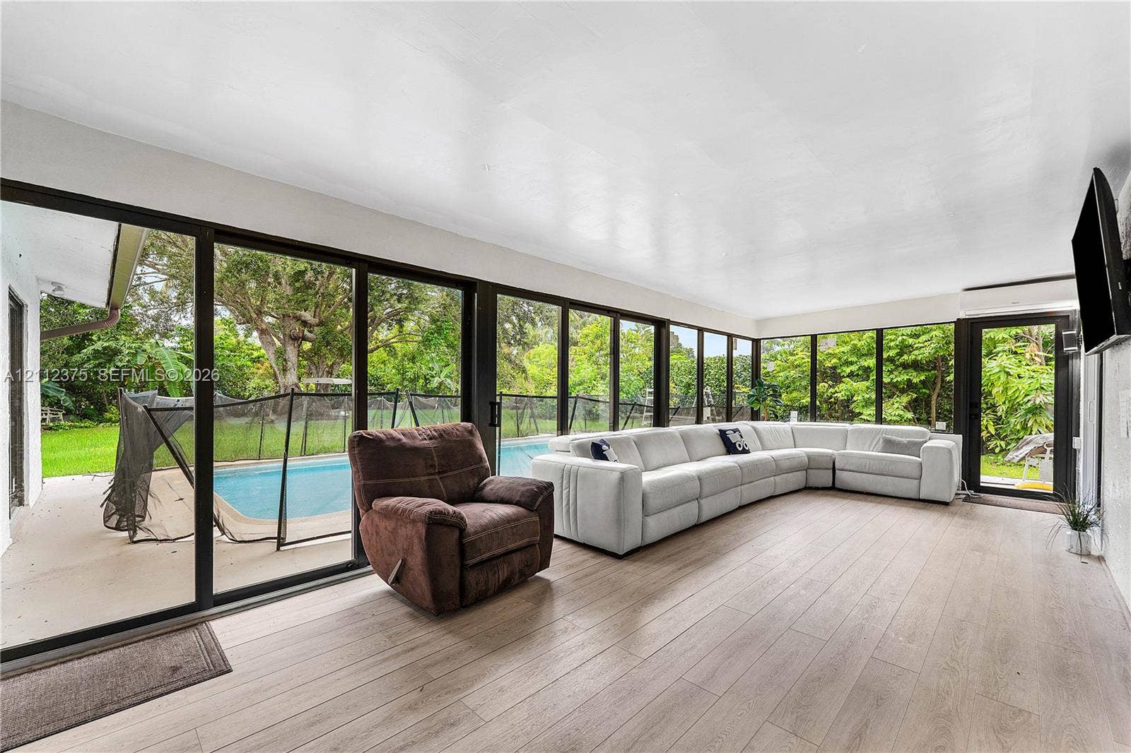 10936 NW 41st Drive, Coral Springs, Coral Springs, FL 33065 Sunroom featuring expansive floor-to-ceiling glass panel walls, wood-finish flooring, and direct access to an exterior swimming pool area