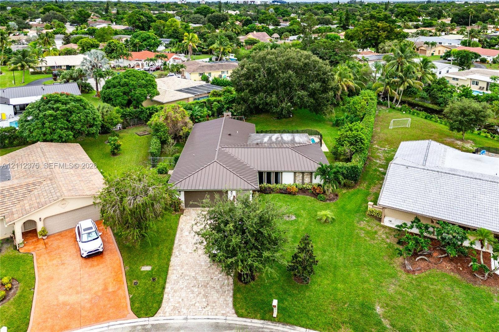 10936 NW 41st Drive, Coral Springs, Coral Springs, FL 33065 Aerial perspective featuring a metal roof, stone-paved driveway, and expansive lawn with mature landscaping