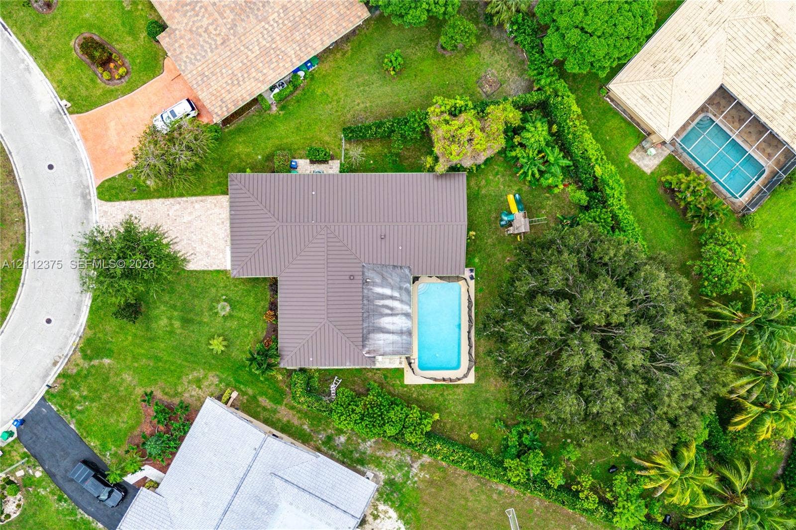 10936 NW 41st Drive, Coral Springs, Coral Springs, FL 33065 Aerial perspective featuring a metal roof, in-ground swimming pool, brick-paver driveway, and mature landscaping