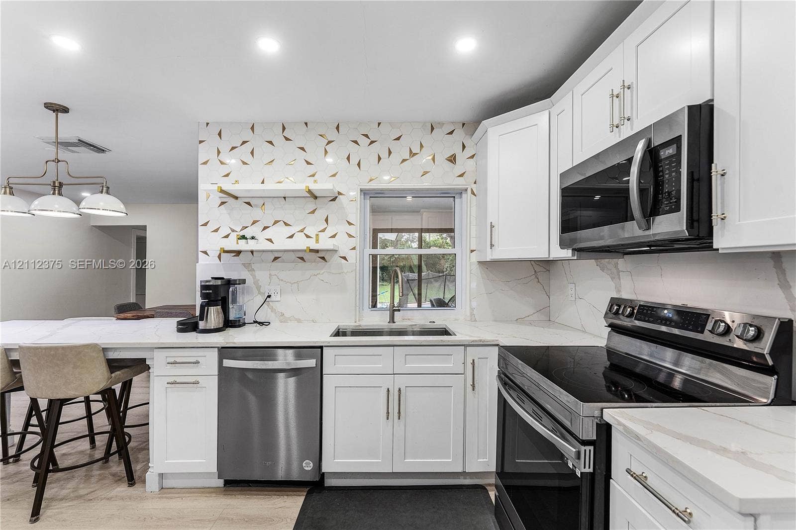 10936 NW 41st Drive, Coral Springs, Coral Springs, FL 33065 Kitchen featuring white shaker-style cabinetry, stainless steel appliances, patterned tile backsplash, floating shelving with metallic accents, and stone-finish countertops
