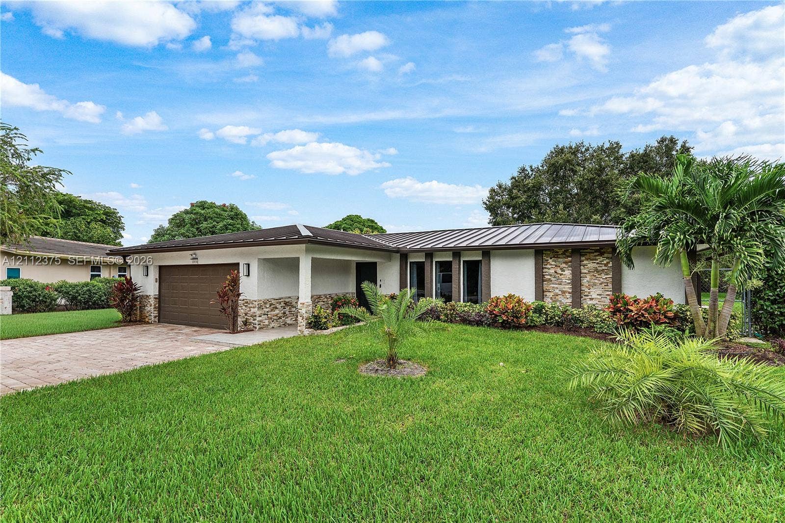 10936 NW 41st Drive, Coral Springs, Coral Springs, FL 33065 Single-story exterior featuring a metal roof, stone-veneer accents, an attached two-car garage, and a brick-paver driveway
