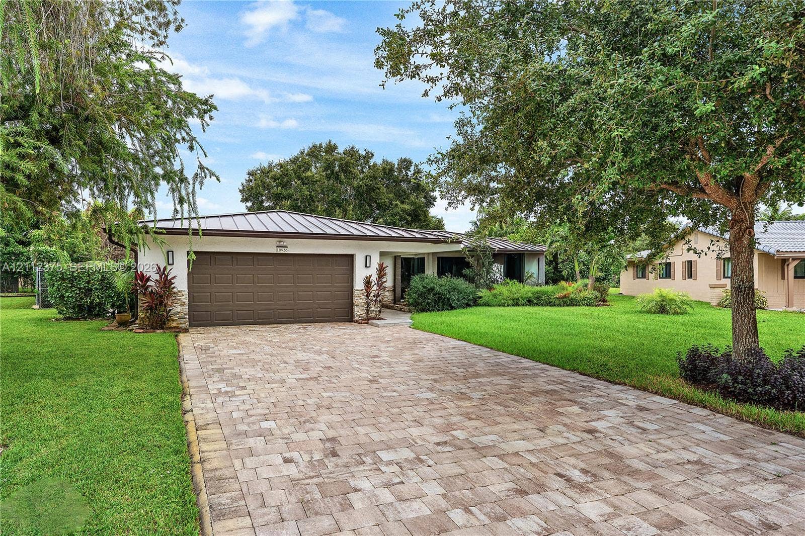 10936 NW 41st Drive, Coral Springs, Coral Springs, FL 33065 Paver driveway leading to a residence featuring a metal roof, two-car garage, and stone-accented exterior