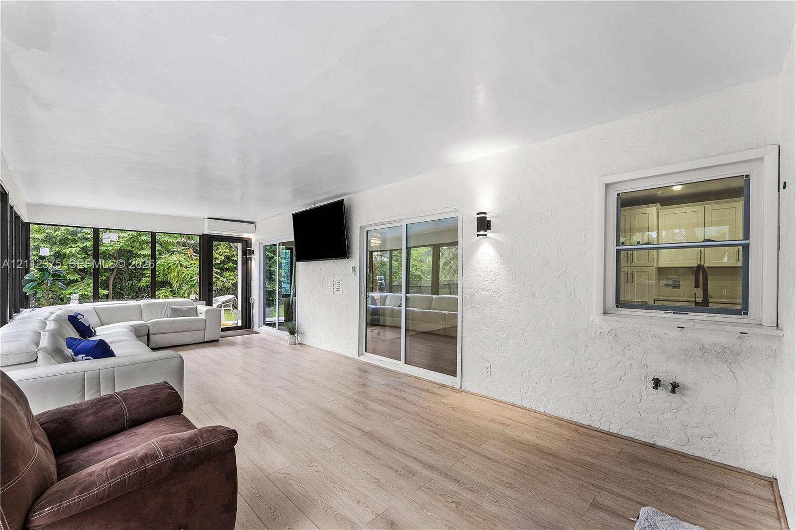 10936 NW 41st Drive, Coral Springs, Coral Springs, FL 33065 Sunroom featuring wood-finish flooring, textured walls, sliding glass doors, wall-mounted light fixtures, and windows with integrated screens
