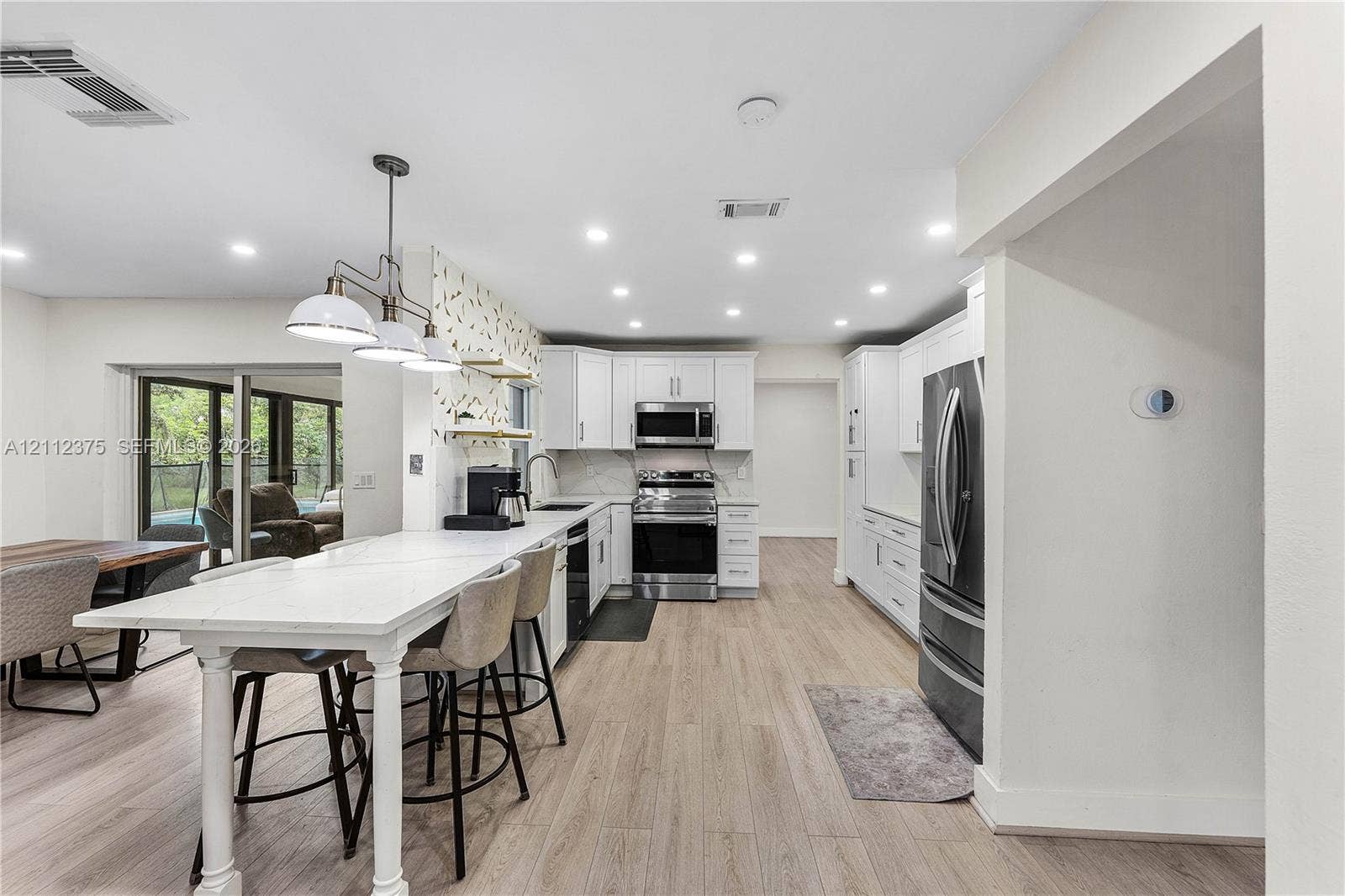 10936 NW 41st Drive, Coral Springs, Coral Springs, FL 33065 Kitchen featuring wood-finish flooring, white cabinetry, integrated stainless steel appliances, and an extended peninsula with a stone-surface countertop