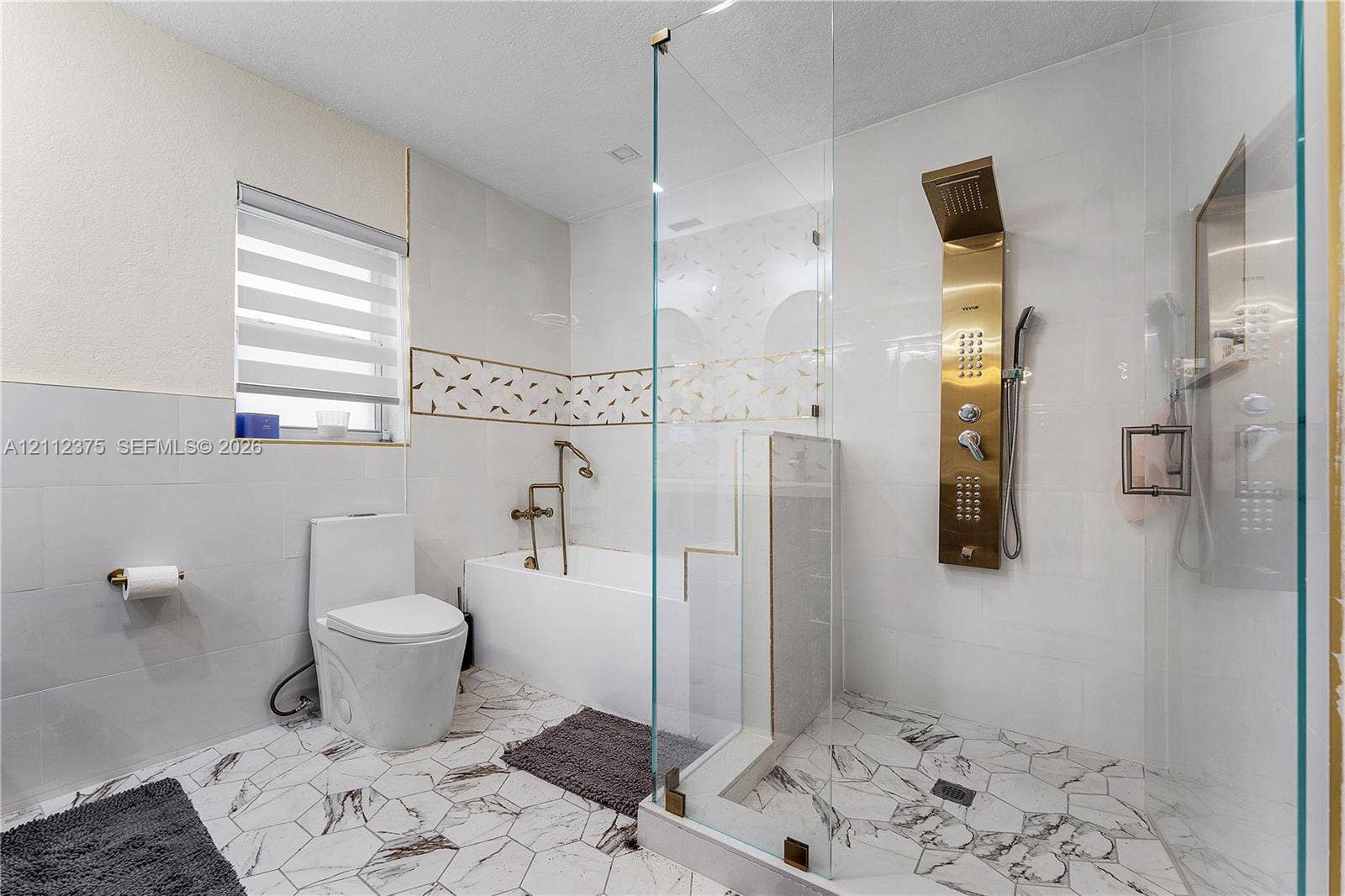 10936 NW 41st Drive, Coral Springs, Coral Springs, FL 33065 Bathroom featuring a walk-in shower with a gold-tone rainfall shower panel, frameless glass enclosure, a deep soaking tub with a wall-mounted faucet, and hexagonal patterned tile flooring