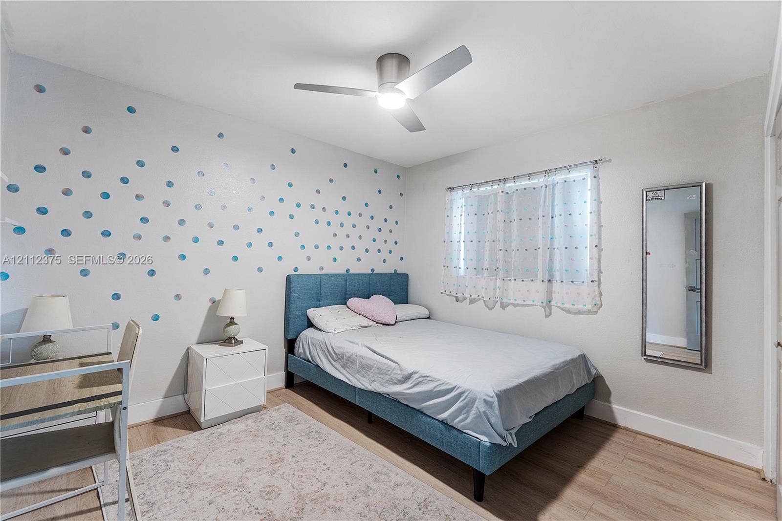 10936 NW 41st Drive, Coral Springs, Coral Springs, FL 33065 Neutral-toned bedroom featuring wood-finish flooring, a contemporary brushed-metal ceiling fan with integrated lighting, and a wall-mounted mirror