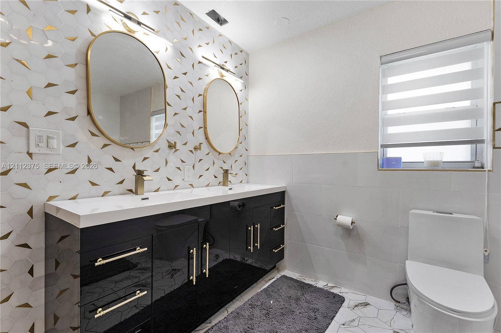 10936 NW 41st Drive, Coral Springs, Coral Springs, FL 33065 Double vanity featuring a high-gloss black cabinet, gold-tone hardware, rectangular integrated sinks, and quartz-finish countertops, accented by geometric patterned wall tile and dual oval gold-framed mirrors
