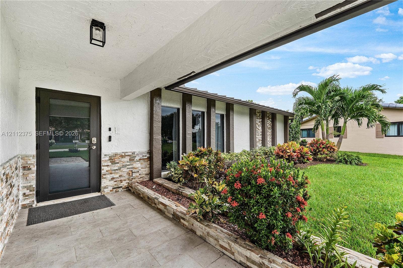 10936 NW 41st Drive, Coral Springs, Coral Springs, FL 33065 Covered entryway featuring stacked stone accents, tile flooring, a glass-panel entry door, and exterior wall-mounted lighting