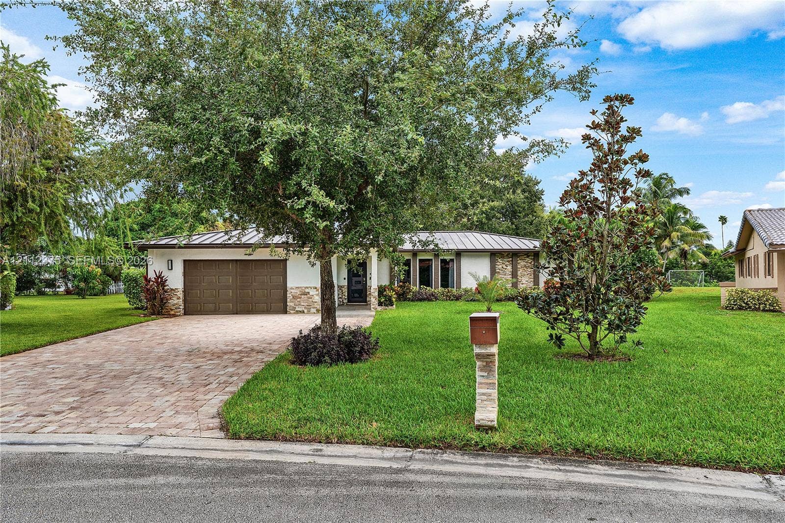 10936 NW 41st Drive, Coral Springs, Coral Springs, FL 33065 Single-story residence featuring a metal roof, paver driveway, two-car garage, stone veneer accents, and extensive lawn landscaping