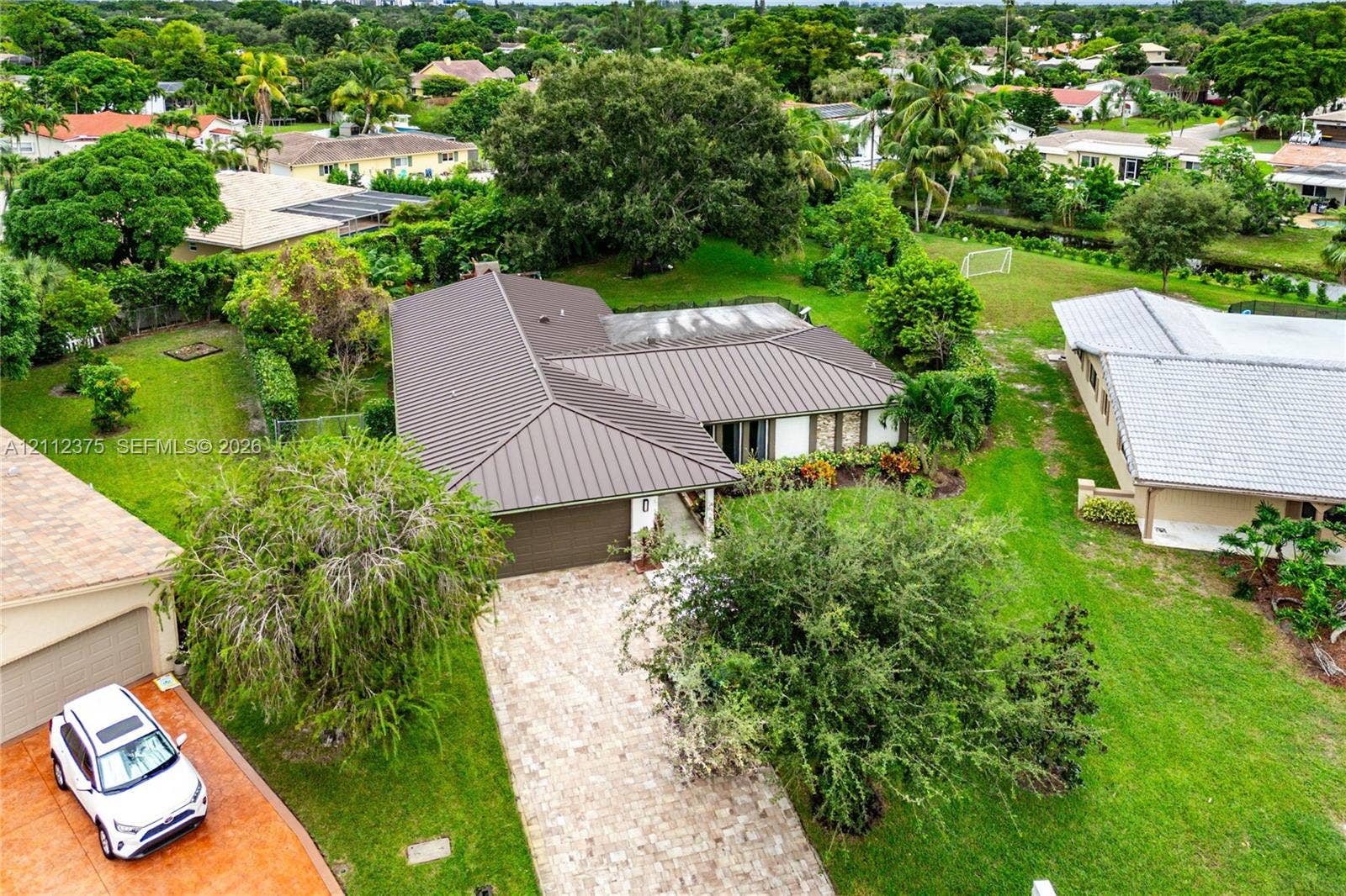 10936 NW 41st Drive, Coral Springs, Coral Springs, FL 33065 Aerial perspective featuring a metal roof, stone-paved driveway, and expansive lawn with mature landscaping