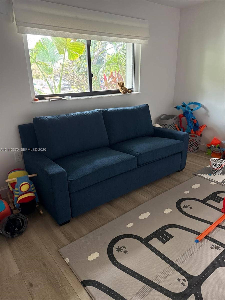 19600 NE 18th Place, Miami, FL 33179 Room featuring wood-finish flooring, a single-hung window with a fabric roller shade, and neutral wall paint
