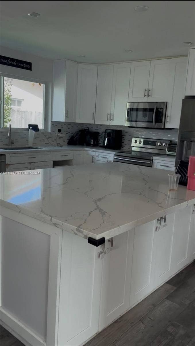 19600 NE 18th Place, Miami, FL 33179 Kitchen featuring a large island with a patterned stone-surface countertop, white shaker-style cabinetry, stainless steel appliances, and wood-finish flooring