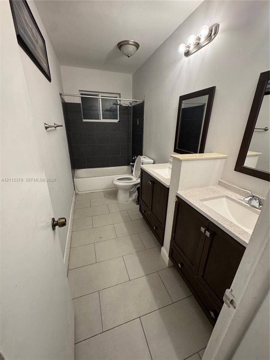 19600 NE 18th Place, Miami, FL 33179 Dual-sink vanity with stone-finish countertops, dark wood cabinetry, and large-format tile flooring, featuring a bathtub with dark tile surround