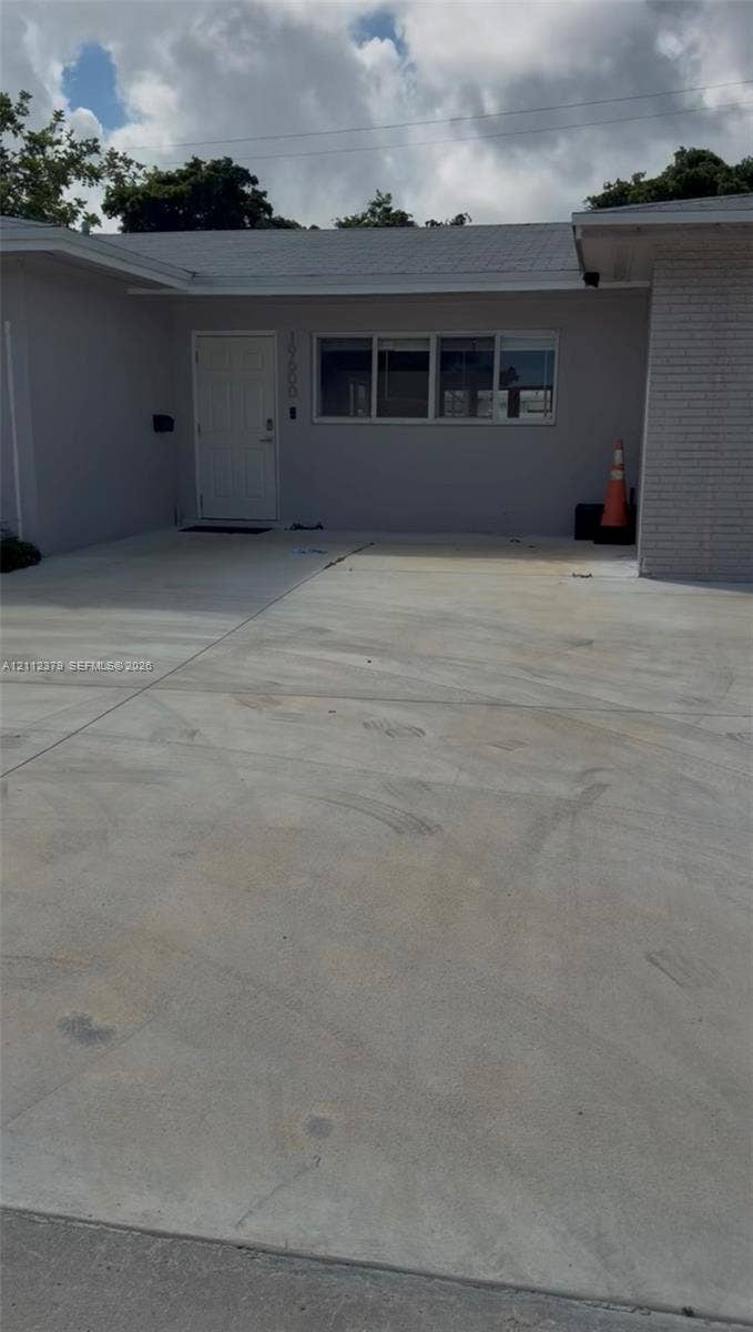 19600 NE 18th Place, Miami, FL 33179 Exterior entrance featuring a concrete driveway, painted stucco facade, brick siding accents, and a panelled entry door