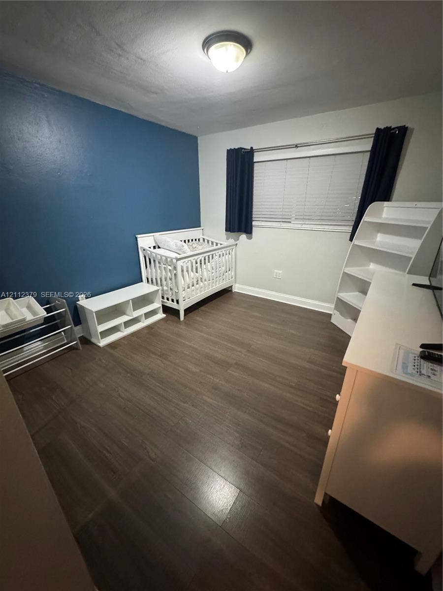 19600 NE 18th Place, Miami, FL 33179 Room featuring wood-finish flooring, a bold accent wall, and a horizontal window with adjustable blinds