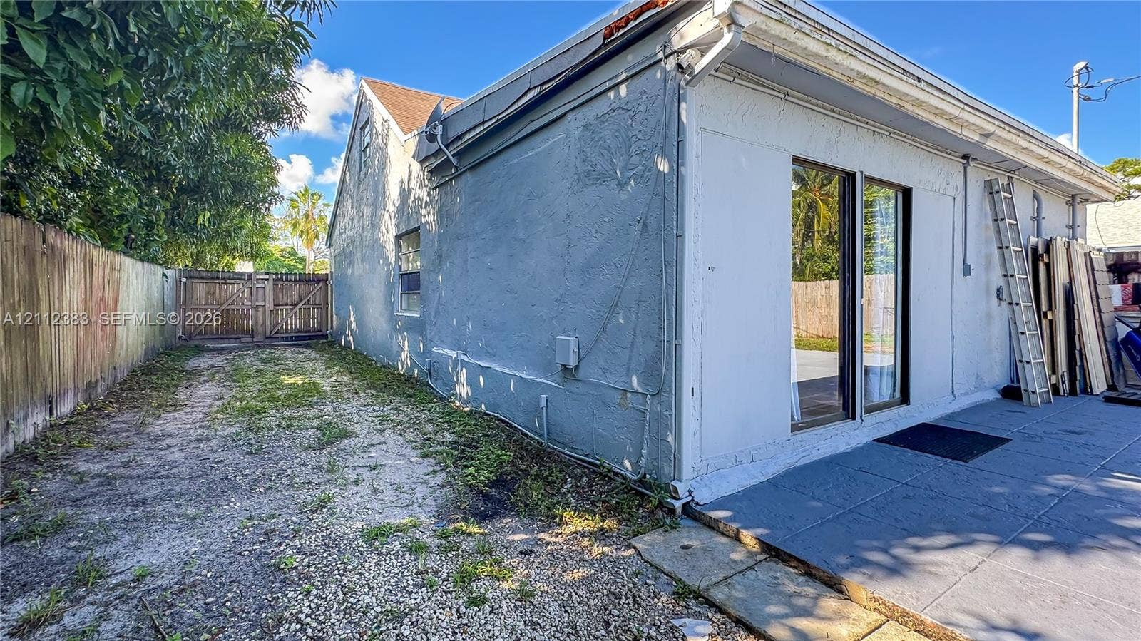 5319 Lake Boulevard, Delray Beach, Delray Beach, FL 33484 Stucco exterior featuring a concrete patio, sliding glass door, and wooden privacy fencing