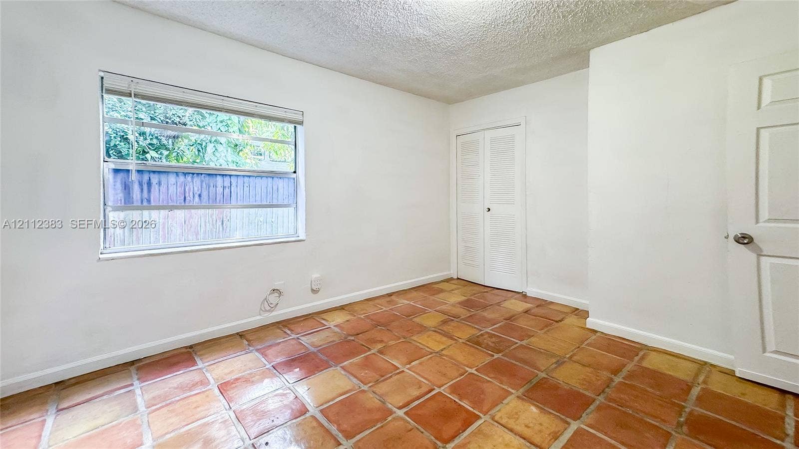 5319 Lake Boulevard, Delray Beach, Delray Beach, FL 33484 Interior room featuring terracotta tile flooring, white walls, dual louvered closet doors, and a single-hung window with a horizontal blind